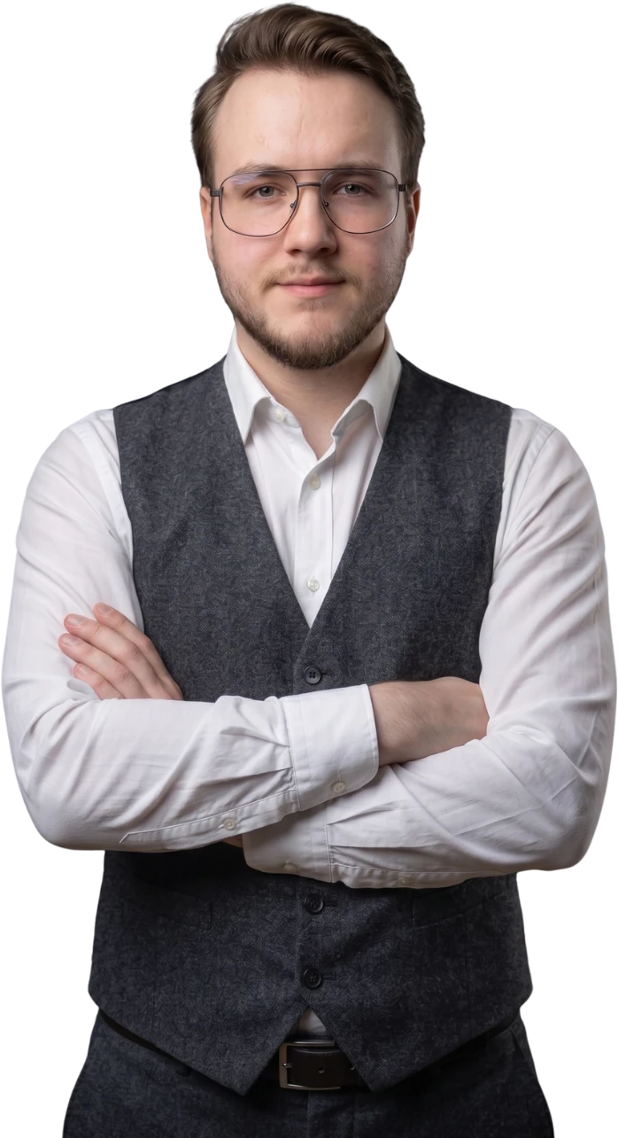 Kacper Mróz w białej koszuli i szarej kamizelce, ze skrzyżowanymi rękami, patrzy w obiektyw